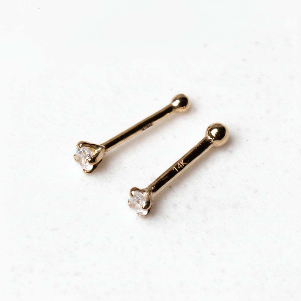 Two gold nose rings with clear gemstones on a white background